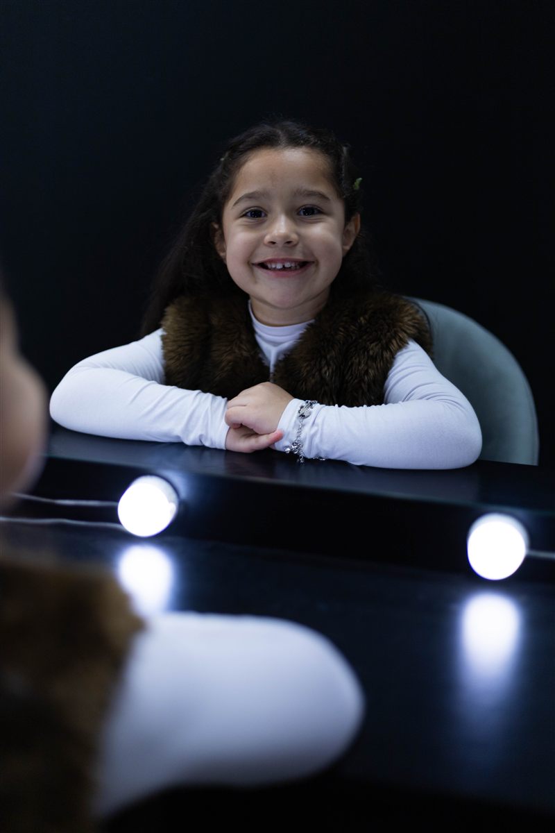 Menina sorrindo diante de um espelho iluminado