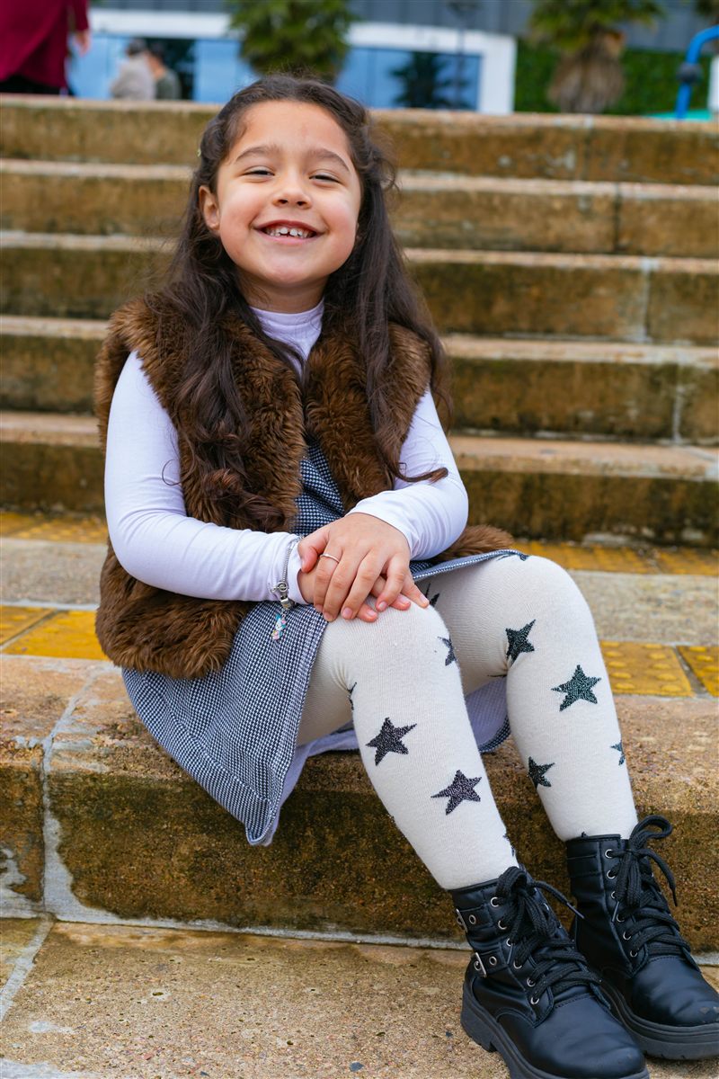 Menina sorrindo sentada em degraus, com colete de pelúcia e meias estampadas de estrelas