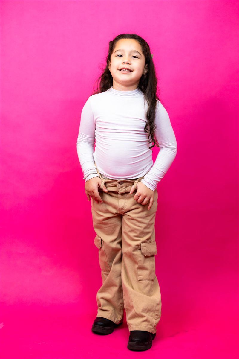 Menina de corpo inteiro com as mãos nos bolsos sobre fundo rosa